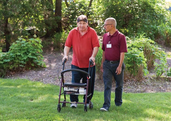 Staff assisting a resident in a lush garden setting