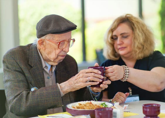 An elderly man being assisted with a beverage by a staff member