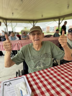 An elderly man giving thumbs up at an outdoor gathering