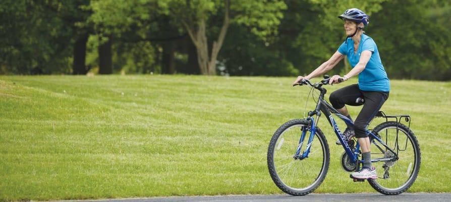 A senior woman riding a bicycle on a grassy path