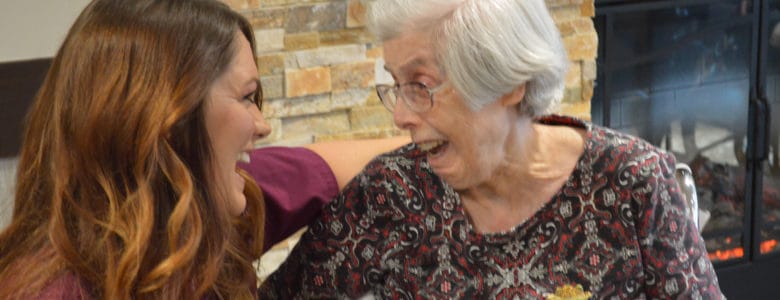 A caregiver laughing with a senior resident by a fireplace