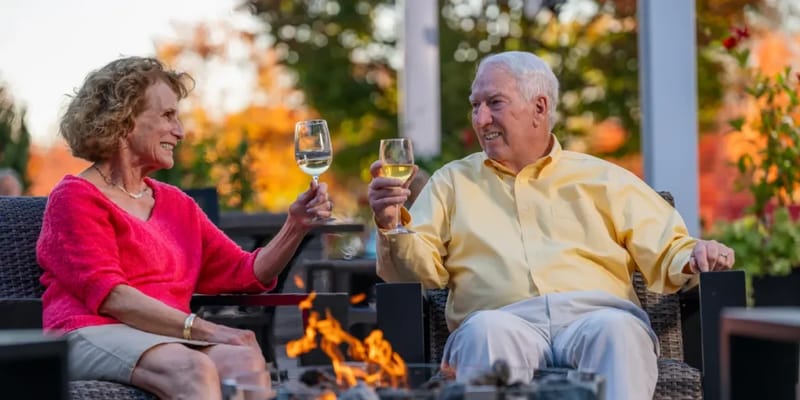 Elderly couple toasting with glasses outdoors by a fire pit