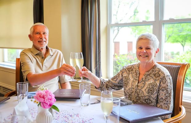 Two residents toasting with drinks at a dining table