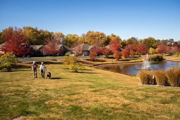 Residents walking by a pond with autumn trees