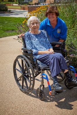 A staff member smiling with a resident in a wheelchair outdoors