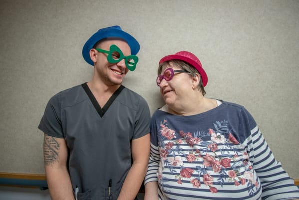 Staff member and resident in playful hats and glasses