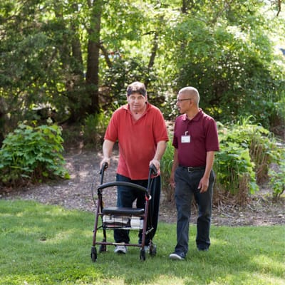 Resident walking in a lush garden with staff assistance
