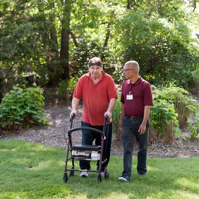 Resident walking in a lush garden with staff assistance