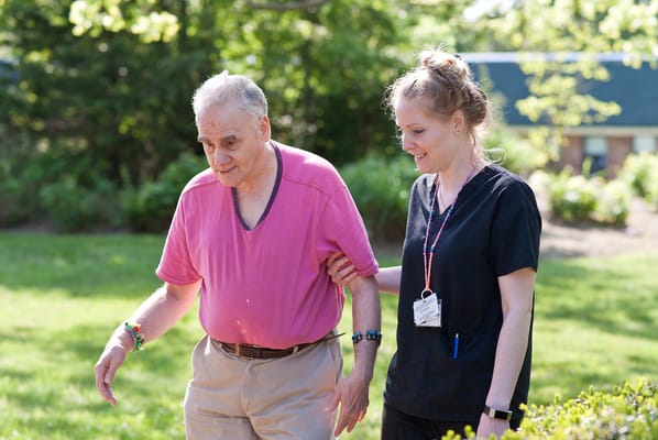 A caregiver assisting an elderly man outdoors