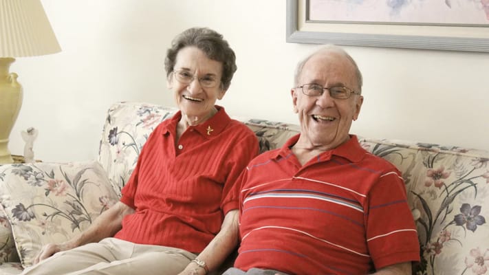 Two smiling seniors sitting comfortably on a sofa