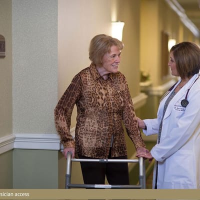 A smiling resident with a walker and a staff member in a hallway