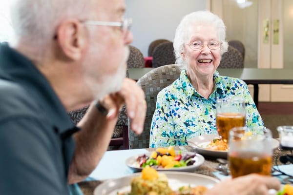 Smiling elderly woman enjoying a meal with a man in a dining setting