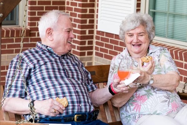Two residents sharing cookies and beverages on a porch swing