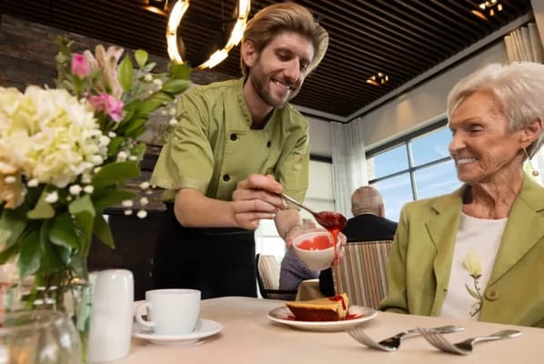 A staff member serving dessert to a resident in the dining area