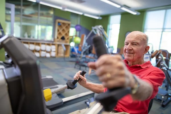 An elderly man exercising on a rowing machine in a fitness room