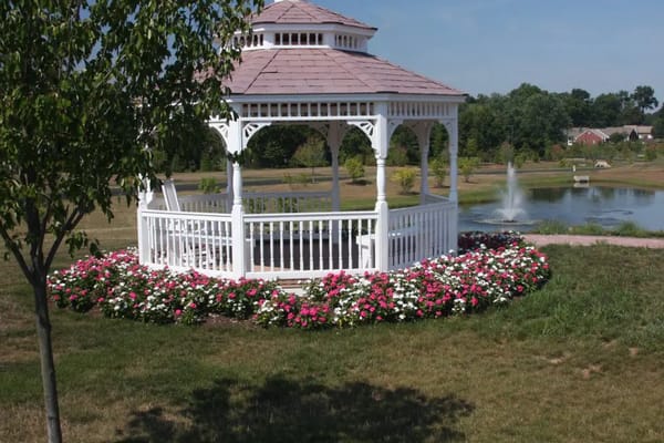 Gazebo surrounded by colorful flowers near a pond