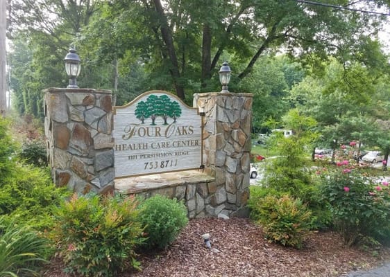 Sign for Four Oaks Health Care Center surrounded by greenery