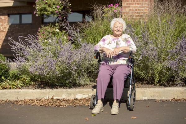 An elderly woman in a wheelchair by purple flowers