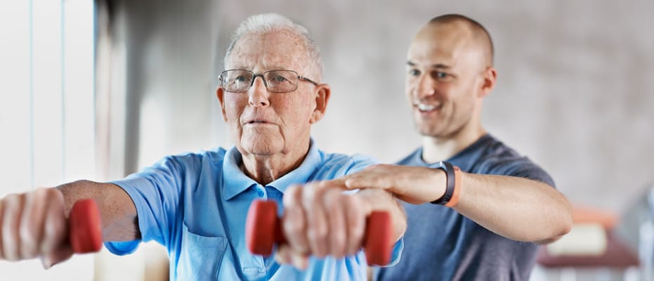 Senior exercising with trainer in gym