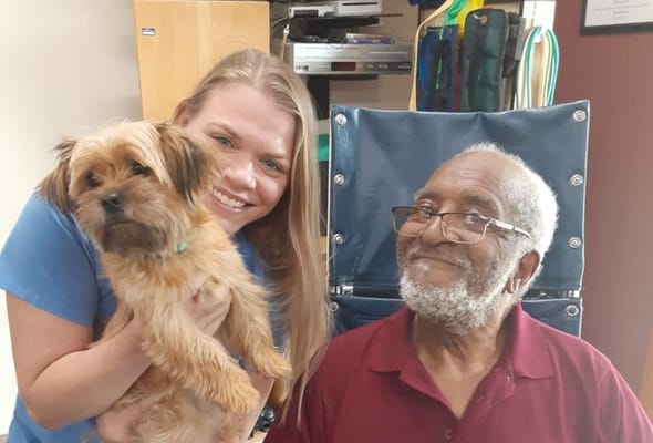 Care staff and a resident smiling with a small dog