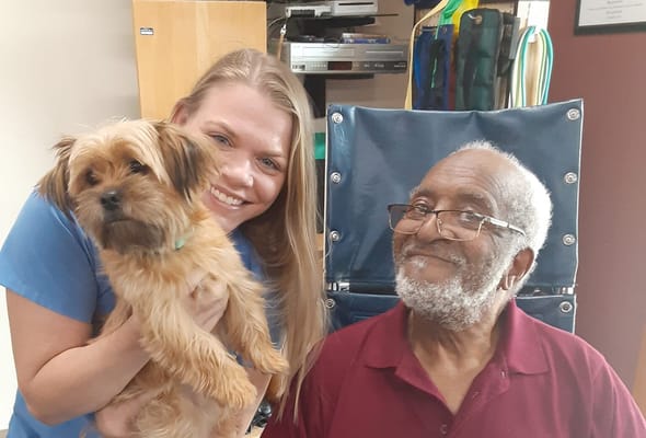 Care staff and a resident smiling with a small dog