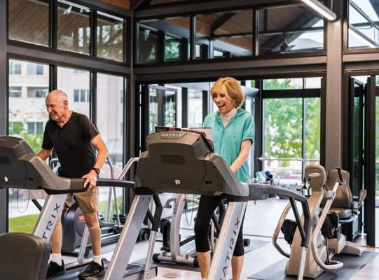 Two residents exercising on treadmills in a fitness area