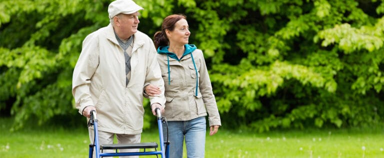 A senior man walking with assistance in a garden