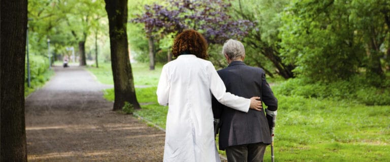 A caregiver assisting a senior in a lush park