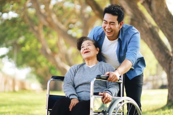 A caregiver pushing a senior resident in a wheelchair outdoors