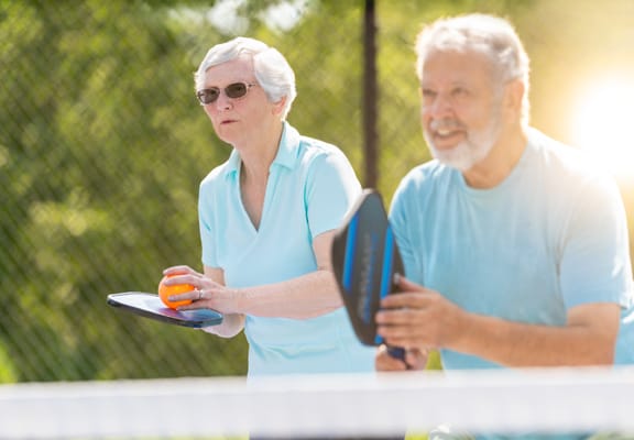 Seniors playing pickleball outdoors in sunny weather