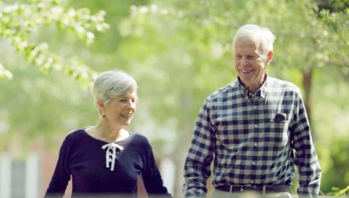 Two seniors walking together in a green outdoor space