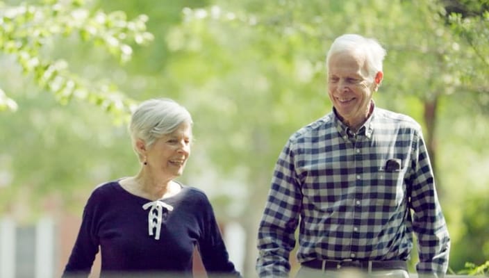 Two seniors walking together in a green outdoor space