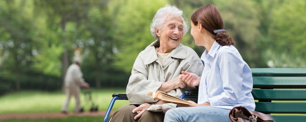 Elderly woman laughing with caregiver on a park bench