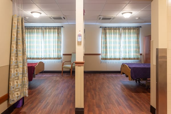 Two empty resident rooms with beds and curtains