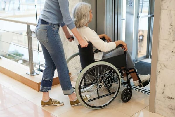 A resident in a wheelchair being assisted in a lobby area