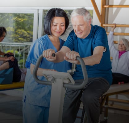Senior exercising with staff assistance in a bright gym