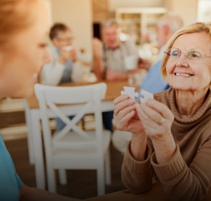 A smiling elderly woman holding puzzle pieces with a caregiver