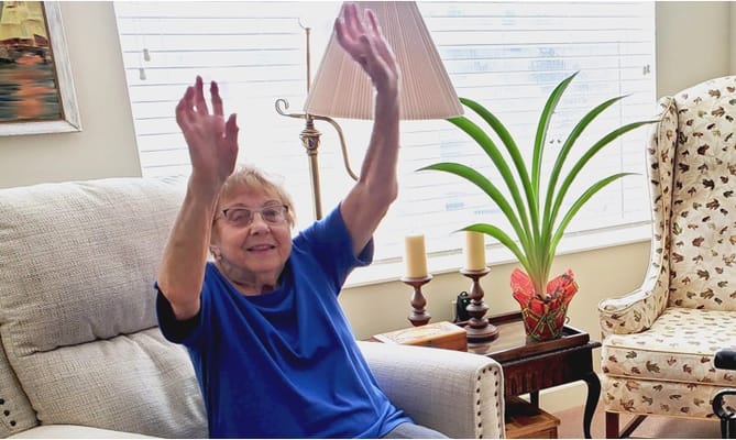 Senior resident joyfully raising hands in a cozy living room