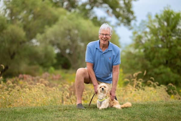 Senior man smiling with a dog in a grassy area