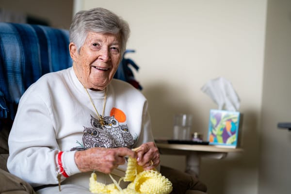 Resident smiling while knitting in a cozy chair