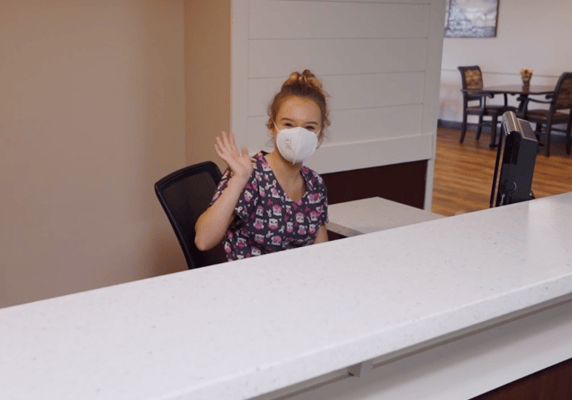 Staff member at the reception desk smiling and waving