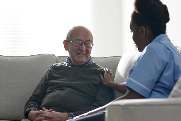A caregiver interacting with an elderly man in a living room