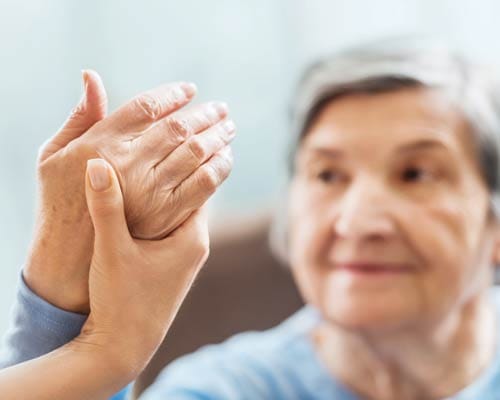 A caregiver holding the hand of an elderly woman