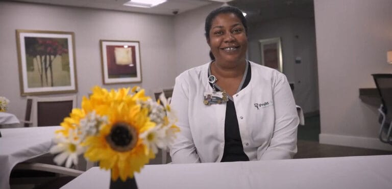 Staff member smiling with a table of flowers in a common area