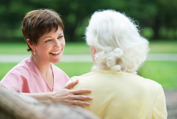 A caregiver interacting with a senior outdoors in a park.