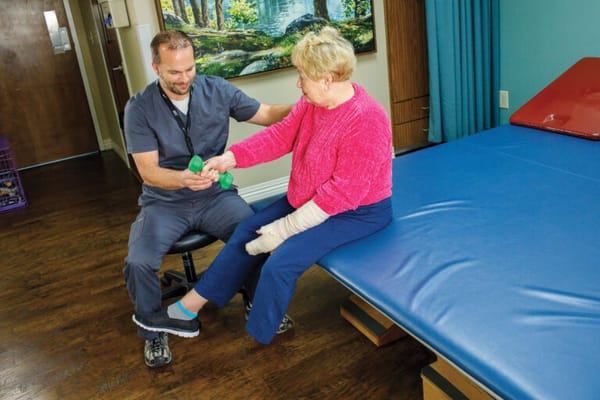 Staff helping a resident with weights in a therapy room