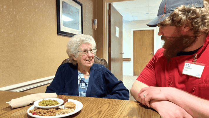An elderly resident talking with staff over a meal.