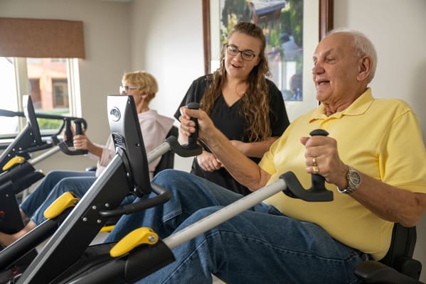 Residents exercising with staff assistance in a fitness area