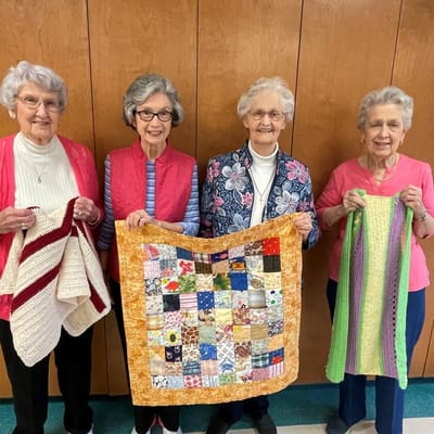 Residents showcasing handmade quilts in an activity room