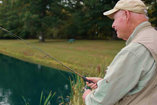 An older man fishing by a serene pond